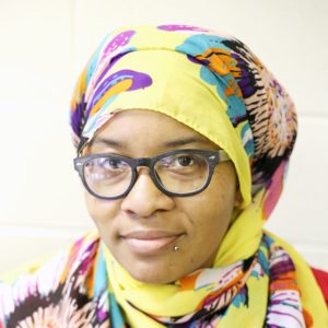 Woman with colorful floral headscarf and glasses looking at the camera.