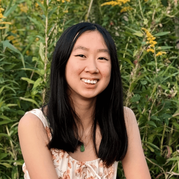 Woman smiling in a garden with green foliage and yellow flowers in the background.