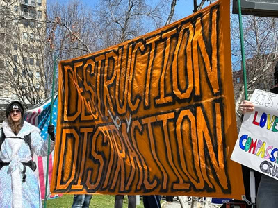 Protest sign reading "Destruction and Displacement" at a rally, related to Iran and immigration frus.