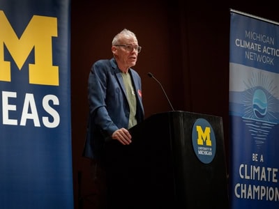 U-M Climate Fellowship event speaker at podium with Michigan and climate banners.