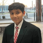 Young boy in formal suit and tie standing outdoors during sunset.
