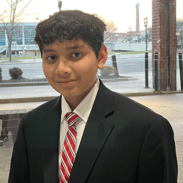 Young boy in formal suit and tie standing outdoors during sunset.