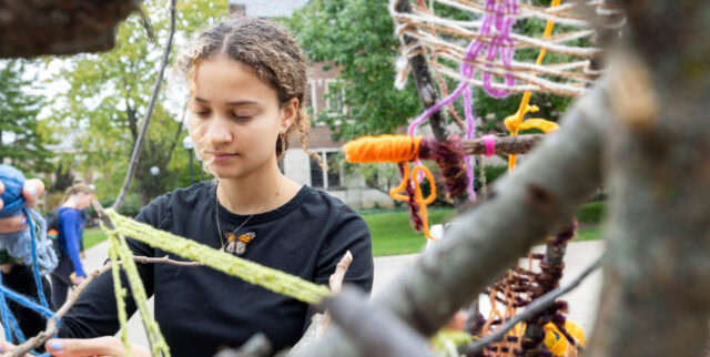 Youth participating in a climate action workshop, tying colorful yarn on branches for environmental awareness in Michigan.
