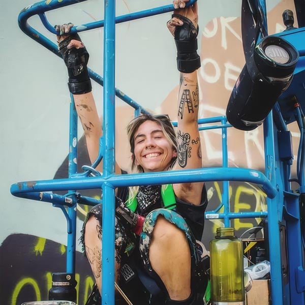 Young woman smiling on outdoor fitness equipment with tattoos and gloves.