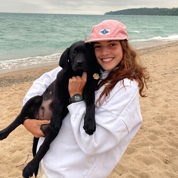 Lyla Hollis on and labrador puppy with woman on a beach, promoting climate action and environmental awareness.