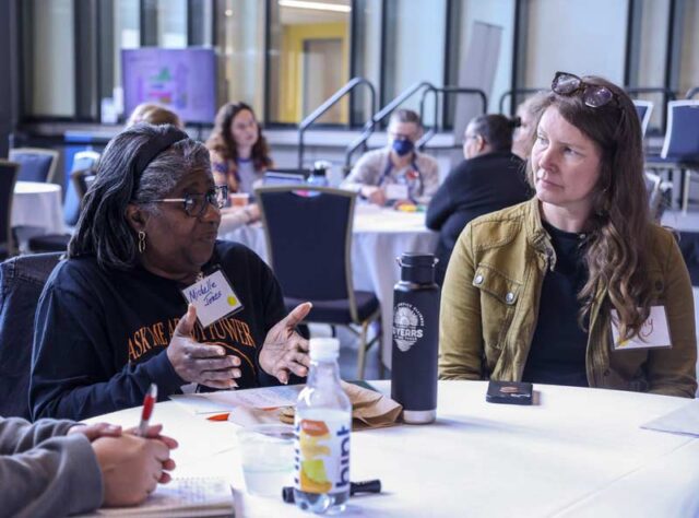 A diverse group of women engaging in a conversation around a table during a networking event at a MiCAN event.