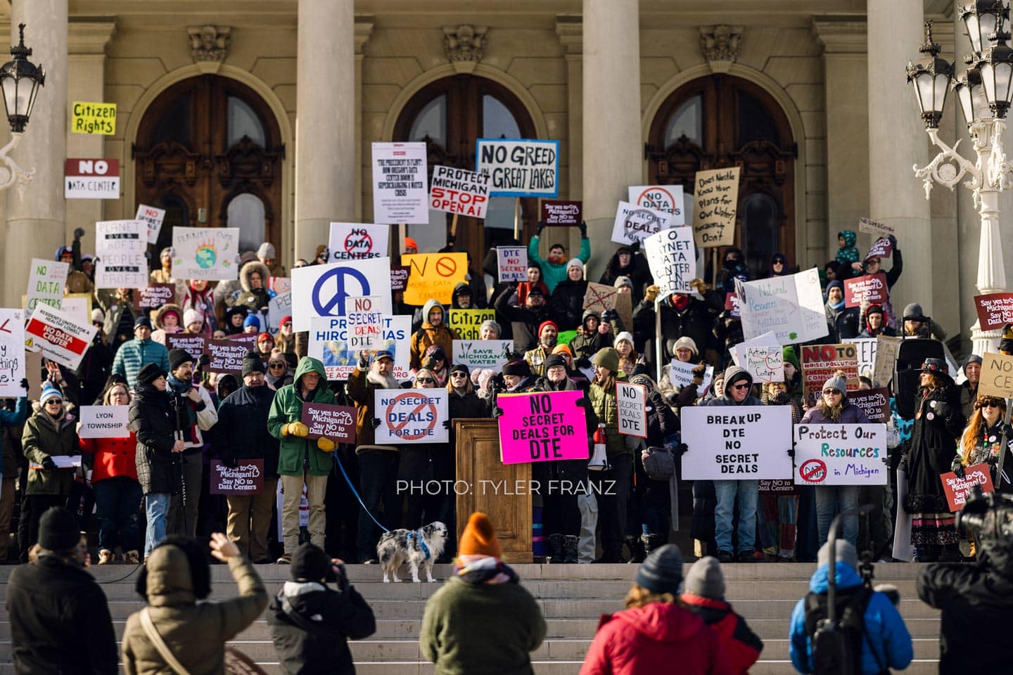 Protesters holding signs against green policies on the steps of a government building.