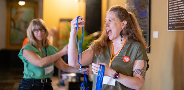 Volunteer event photo showing a woman smiling and holding blue ribbons at an indoor event.